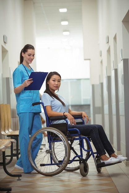 Infermiera femminile che assiste il paziente sulla sedia a rotelle in corridoio