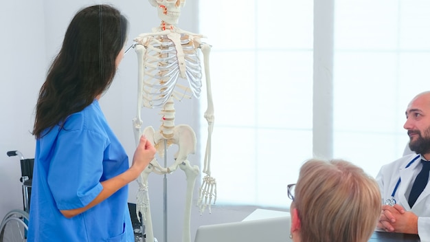 Infermiera femminile che dimostra sullo scheletro davanti ai chirurghi medici nella sala conferenze. Terapista esperto della clinica che parla con i colleghi della malattia, professionista della medicina