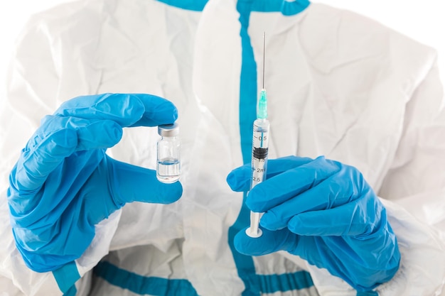 Infermiera medica in DPI e guanti in lattice che tengono una siringa con un vaccino covid-19. Coronavirus, pandemia e concetto di salute.