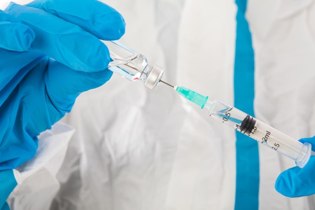 Infermiera medica in DPI e guanti in lattice che trasportano una siringa con un vaccino covid-19. Coronavirus, pandemia e concetto di salute.