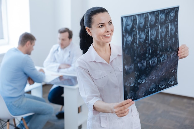 Infermiera sorridente felice professionale che lavora e analizza la scansione mrt mentre il medico consulta il paziente dietro