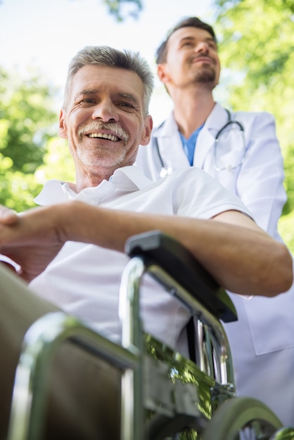 Infermiere che cammina con il paziente senior in sedia a rotelle in giardino.