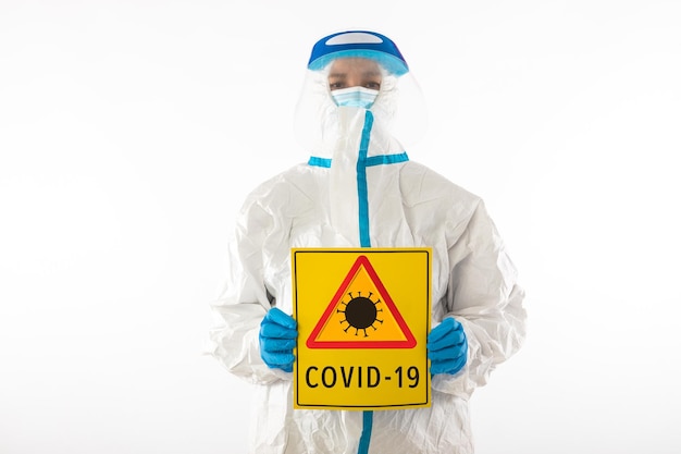 Infermiere medico che indossa un DPI e guanti in lattice con un cartello giallo con un simbolo di pericolo di coronavirus che dice: "COVID-19". Coronavirus, pandemia e concetto di salute.