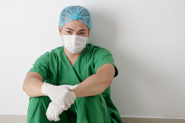 Infermiere medico maschio stanco in guanti protettivi seduto nel corridoio dell'ospedale durante una breve pausa a