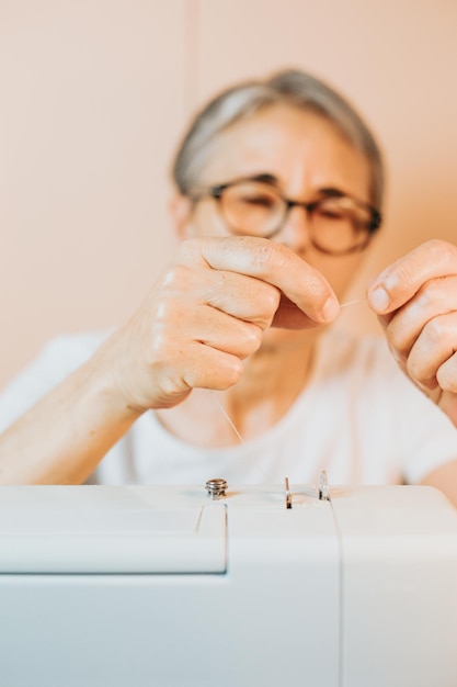 Infilatura della mano della donna che prepara l'ago nell'ago della macchina da cucireLa donna anziana cuce su un cucito d'epocaVecchi nuovi hobby a casa anziani attività mentale e lavoroVecchia sarta