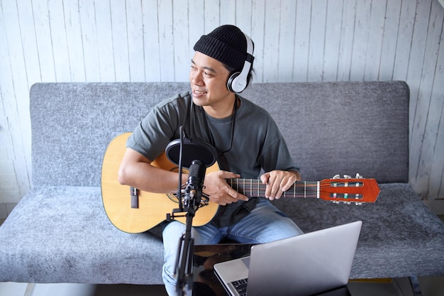 Influencer asiatico che suona la chitarra durante il podcast o la trasmissione video in diretta nello studio di casa