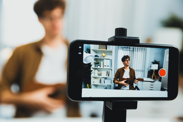 Influencer che canta e suona la chitarra si concentra sulla vista del telefono sullo sfondo sfocato Gusher