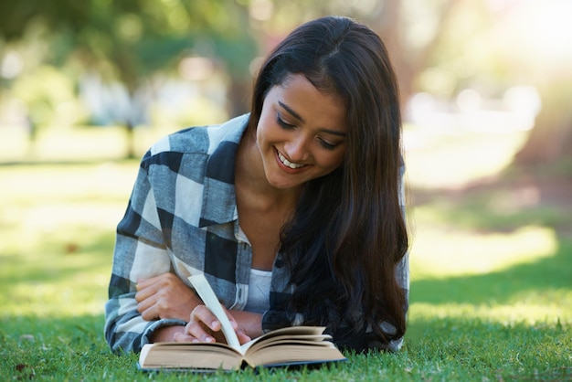 Informazioni femminili e libri di lettura sulla letteratura dell'erba e sorridendo per la narrativa di finzione o fantasia Persona femminile natura e rilassarsi sul prato per la conoscenza romanzo e studente che studia in giardino