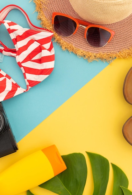 Infradito, cappellino, bikini e macchina fotografica su giallo e blu. concetto di spazio della copia di viaggio di divertimento di vacanza estiva.