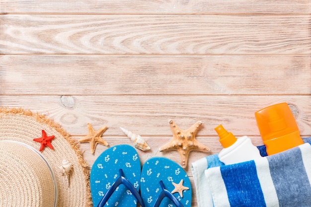 Infradito, cappello di paglia, stelle marine, bottiglia di crema solare, lozione per il corpo spray su fondo in legno vista dall'alto. piatto laici estate spiaggia mare accessori sfondo, concetto di vacanza.