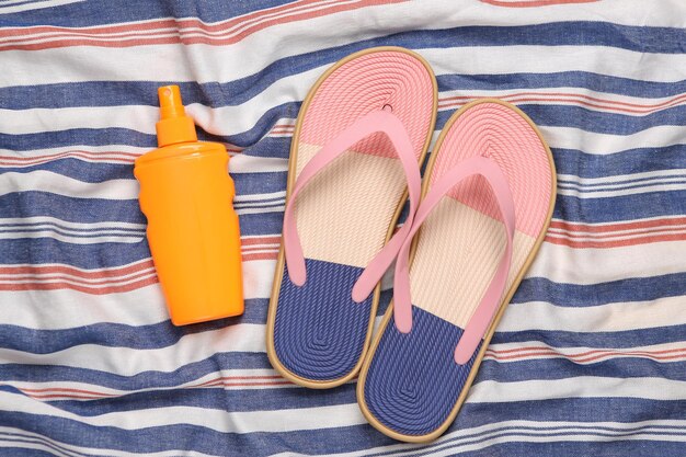 Infradito e bottiglia di crema solare su una superficie a strisce Concetto di vacanza al mare
