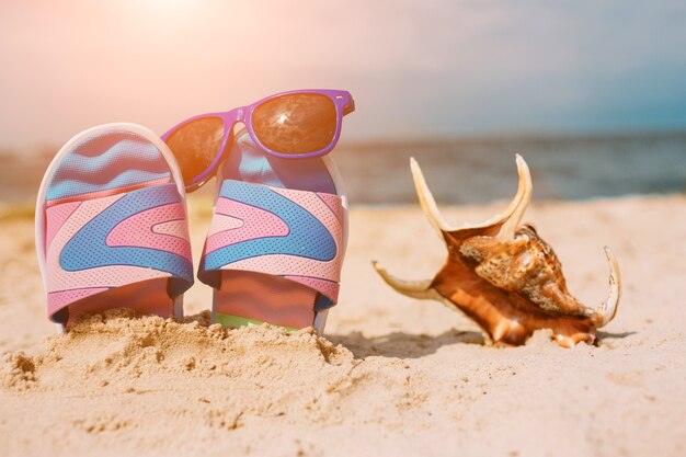 Infradito nella sabbia sulla spiaggia. Occhiali da sole su di esso. Concetto di vacanza estiva. Riva del mare