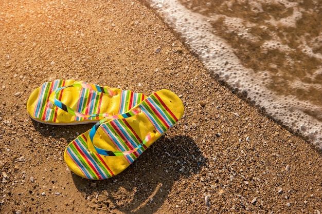 Infradito su sfondo sabbia Le calzature a terra vanno all'estate al mare sull'isola tropicale