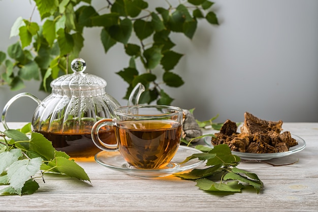 Infuso curativo di funghi di betulla chaga in coppe di vetro e pezzi di chaga su un tavolo di legno