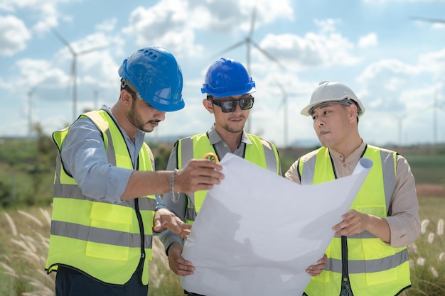 Ingegnere asiatico che lavora nel lavoro sul campo all'aperto I lavoratori controllano e ispezionano la costruzione e la macchina intorno al sito del progetto di costruzione Turbina eolica per l'elettricità di energia pulita e sostenibile per l'ambiente