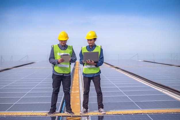 Ingegnere asiatico del team in piedi sulla fabbrica sul tetto e controllando l'energia solare delle celle solari mediante la tecnologia dei tablet
