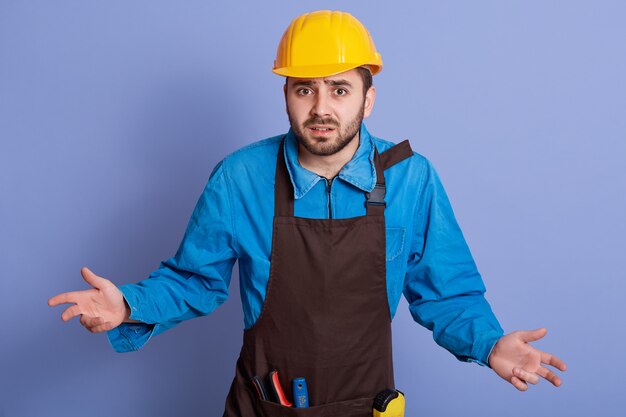 Ingegnere barbuto indifeso che indossa il casco protettivo giallo allargando le mani ai lati