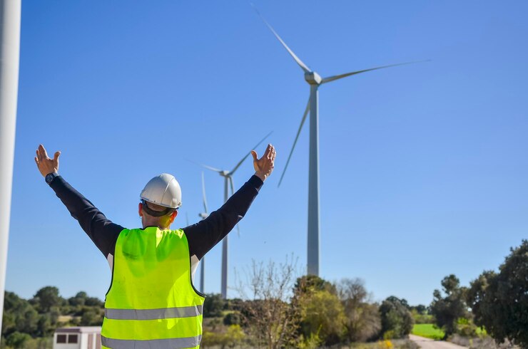 Foto ingegnere che alza le braccia davanti alle turbine eoliche per festeggiare le energie rinnovabili