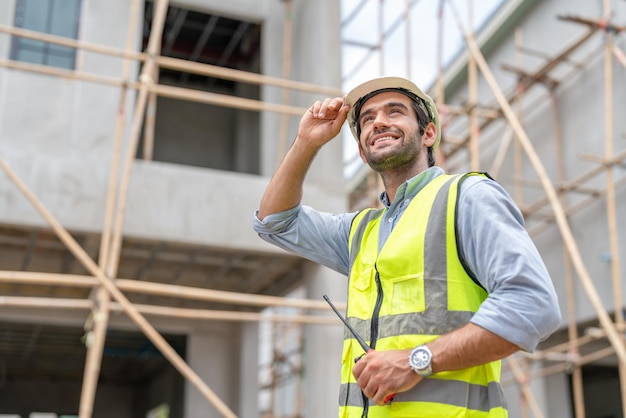 Ingegnere civile maschio che tiene il walkie-talkie che cammina per l'ispezione del complesso residenziale al cantiere