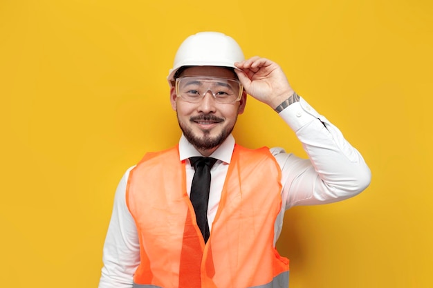Ingegnere costruttore asiatico in uniforme su sfondo giallo isolato Uomo coreano maschio con elmetto