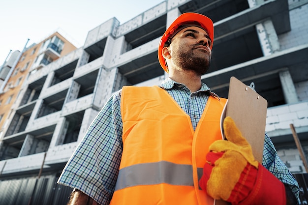 Ingegnere del giovane in abiti da lavoro in piedi in cantiere con appunti