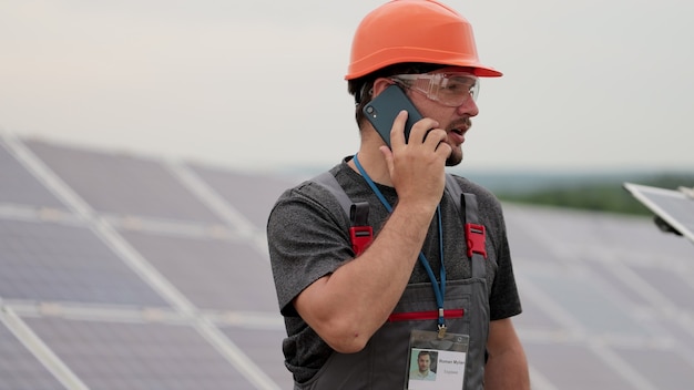 Ingegnere dell'uomo che parla al telefono. Giovane maschio che lavora in remoto tra file di pannelli solari. Campo di pannelli solari. Produzione di energia pulita. Energia verde.