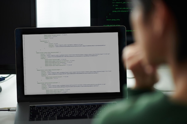 Ingegnere Devops che guarda il codice di programmazione sullo schermo di un portatile e di un computer