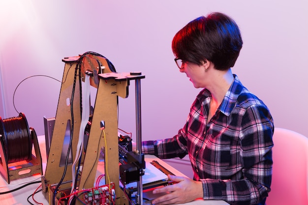 Ingegnere donna che lavora di notte in laboratorio, sta regolando i componenti di una stampante