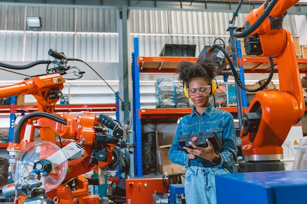 Ingegnere donna intelligente lavoratore che lavora programmazione saldatrice robotica Ragazza adolescente nera lavora in anticipo in fabbrica moderna