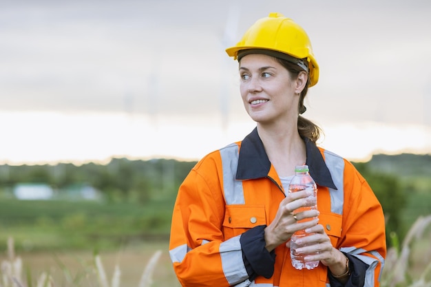 Ingegnere donna tecnico in piedi rilassarsi riposare bere acqua pulita dopo aver finito la manutenzione della turbina eolica generatore di energia