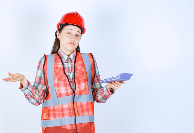 Ingegnere femminile in casco rosso che lavora alla calcolatrice e sembra confuso o entusiasta.