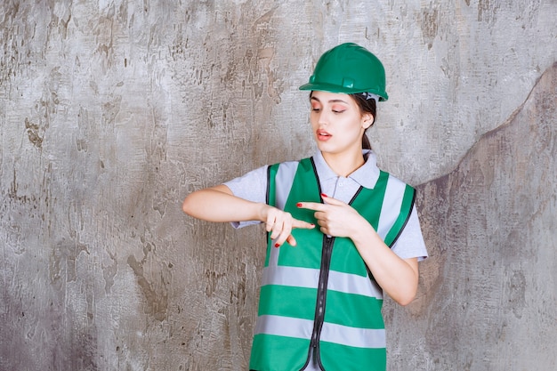 Ingegnere femminile in uniforme verde e casco che mostra il tempo.