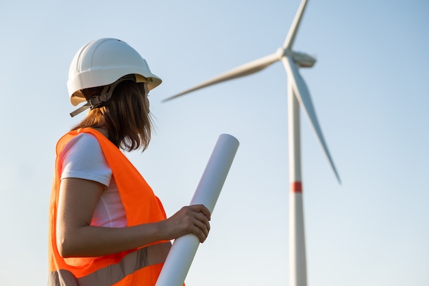 Ingegnere in elmetto e giubbotto protettivo tiene un progetto di piano per la costruzione di turbine eoliche