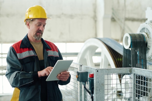 Ingegnere in uniforme che controlla il lavoro della macchina con tablet pc in fabbrica