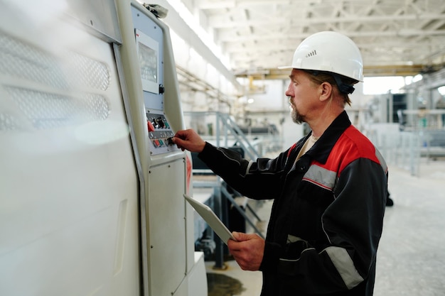 Ingegnere in uniforme e elmetto protettivo che imposta il lavoro della macchina utilizzando la tavoletta digitale