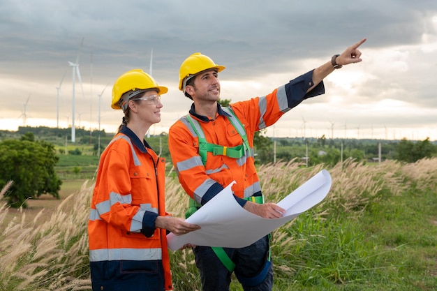 Ingegnere intelligente con casco protettivo che tiene in mano il progetto che lavora nel campo delle turbine elettriche