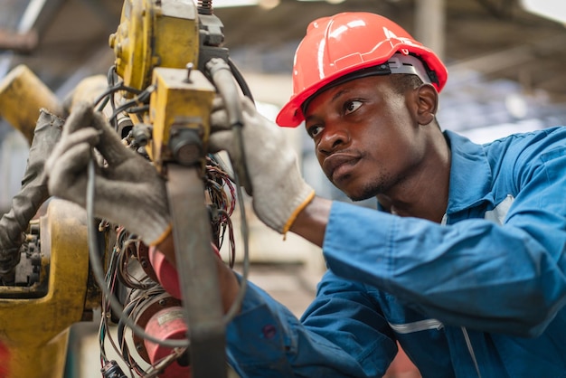 Ingegnere maschio afroamericano che controlla e ripara il vecchio braccio robotico in fabbrica Industriale