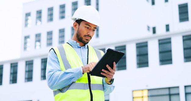 Ingegnere maschio che controlla i dati sulla tavoletta digitale e ispeziona il tecnico del cantiere in un elmetto protettivo che fa la gestione e la pianificazione del progetto all'aperto Lavoratore esperto che osserva o supervisiona le operazioni