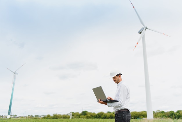 Ingegnere maschio con elmetto che lavora presso l'impianto di turbine eoliche su laptop