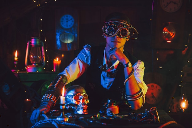 Ingegnere maschio con occhiali cyberpunk e un abito steampunk in un'officina con una luce al neon