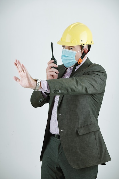 Ingegnere maturo in maschera e casco da lavoro che parla alla radio mentre lavora in cantiere