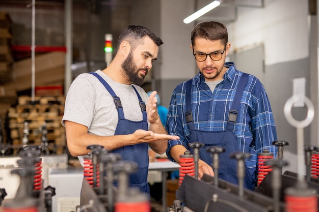 Ingegnere meccanico professionista che dà istruzioni al suo apprendista mentre mostra nuove attrezzature industriali in officina