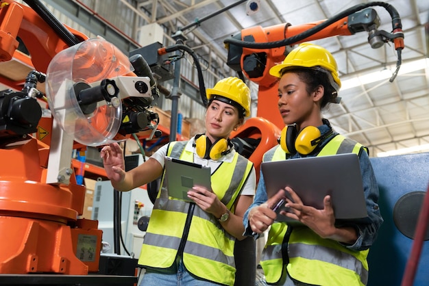 Ingegneri di automazione femminile che utilizzano il computer portatile per l'ispezione della nuova macchina del braccio del robot di saldatura in fabbrica