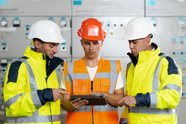 Ingegneri in uniforme e caschi con tablet digitale eseguono lavori di precommissioning ispezioni elettriche