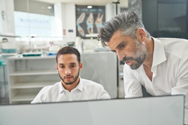 Ingegneri maschi professionisti barbuti concentrati in abbigliamento formale che navigano al computer mentre discutono del progetto durante il lavoro in un ufficio moderno e spazioso