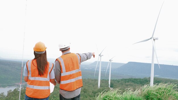 Ingegneri maschili e femminili che lavorano in un parco eolico in cima a una collina o montagna nel progressivo rurale ideale per la futura produzione di energia rinnovabile sostenibile