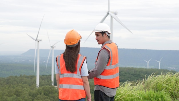 Ingegneri uomini e donne che lavorano in un parco eolico in cima a una collina o montagna nell'ideale progressista rurale per la futura produzione di energia rinnovabile e sostenibile