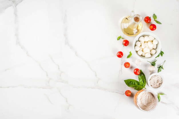 Ingrediente alimentare italiano della pizza casalinga della pasta sulla tavola di marmo bianca con la vista superiore degli accessori della farina, dell'olio d'oliva, del basilico, dei pomodori e della cucina