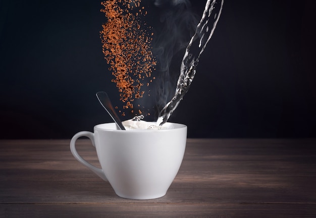 Ingrediente per caffè in una tazza bianca e caffè macinato in aria su uno sfondo scuro.