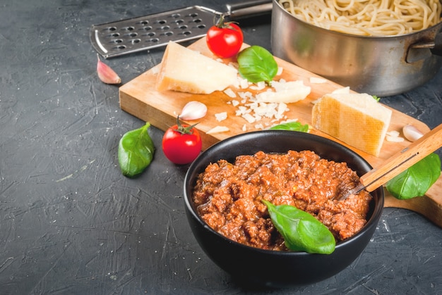 Ingredienti della cucina italiana. Prodotti per la preparazione della pasta alla bolognese, il processo di cottura. Spaghetti saldati in padella, ragù alla bolognese, basilico, aglio, pomodoro, parmigiano